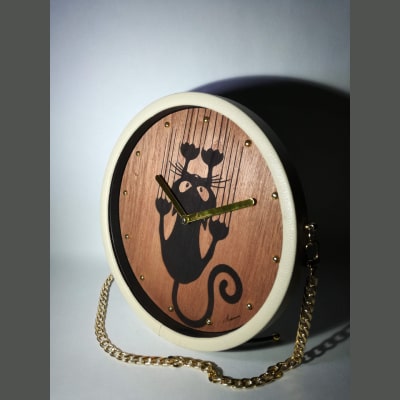 Orologio da scrivania in legno di noce con incisione a laser di un gatto che graffia la parete. Dettagli dorati su lancette e numeri, cornice in ecopelle beige e tracolla in metallo dorato. Articolo artigianale, unico e raffinato, perfetto come regalo originale per ogni occasione.