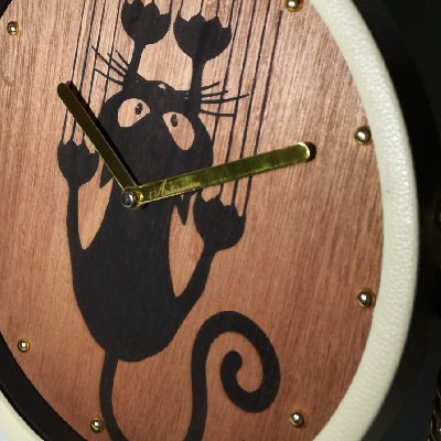 Particolare: Orologio da scrivania e da scrivania in legno di noce con incisione a laser di un gatto che graffia la parete. Dettagli dorati su lancette e numeri, cornice in ecopelle beige e tracolla in metallo dorato. Articolo artigianale, unico e raffinato, perfetto come regalo originale per ogni occasione.