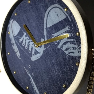 Particolare: Orologio unico con sneakers incise su jeans, cornice in ecopelle bianca, lancette dorate e tracolla in metallo. Stile originale per casa, ufficio o regalo speciale.