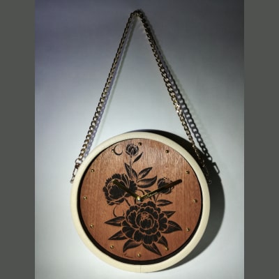 Orologio da parete moderno con incisione di romantiche rose su noce, lancette dorate, cornice in ecopelle beige e tracolla dorata. Eleganza artigianale per ogni spazio.