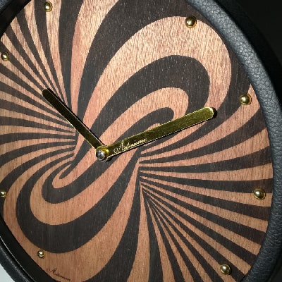 Particolare: Orologio in legno di noce con immagine di vortice inciso a laser, dettagli dorati, cornice in ecopelle nera e tracolla dorata. Elegante e innovativo.