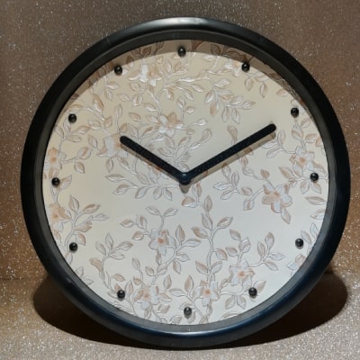 Un orologio da parete di design, unico nel suo genere, con corpo beige, dettagli floreali in madreperla e quadrante nero. Un connubio perfetto tra estetica e funzionalità, trasformando il tempo in un'opera d'arte.