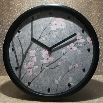 L'orologio grigio moderno con rami e fiori di pesco rosa unisce eleganza e natura. La base neutra, il design in rilievo e le lancette nere creano un equilibrio perfetto. Un regalo unico per aggiungere serenità e stile all'arredamento.