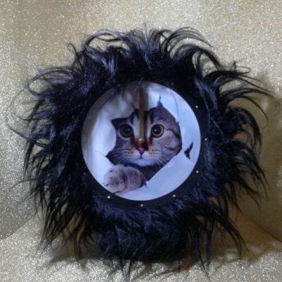 Secondo particolare: Orologio da parete con adorabile gatto tigrato, bordo in pelliccia sintetica nera. Un’idea regalo originale che aggiunge gioia e originalità agli ambienti.