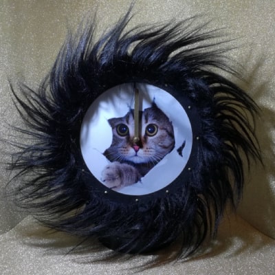 Primo particolare: Orologio da parete con adorabile gatto tigrato, bordo in pelliccia sintetica nera. Un’idea regalo originale che aggiunge gioia e originalità agli ambienti.